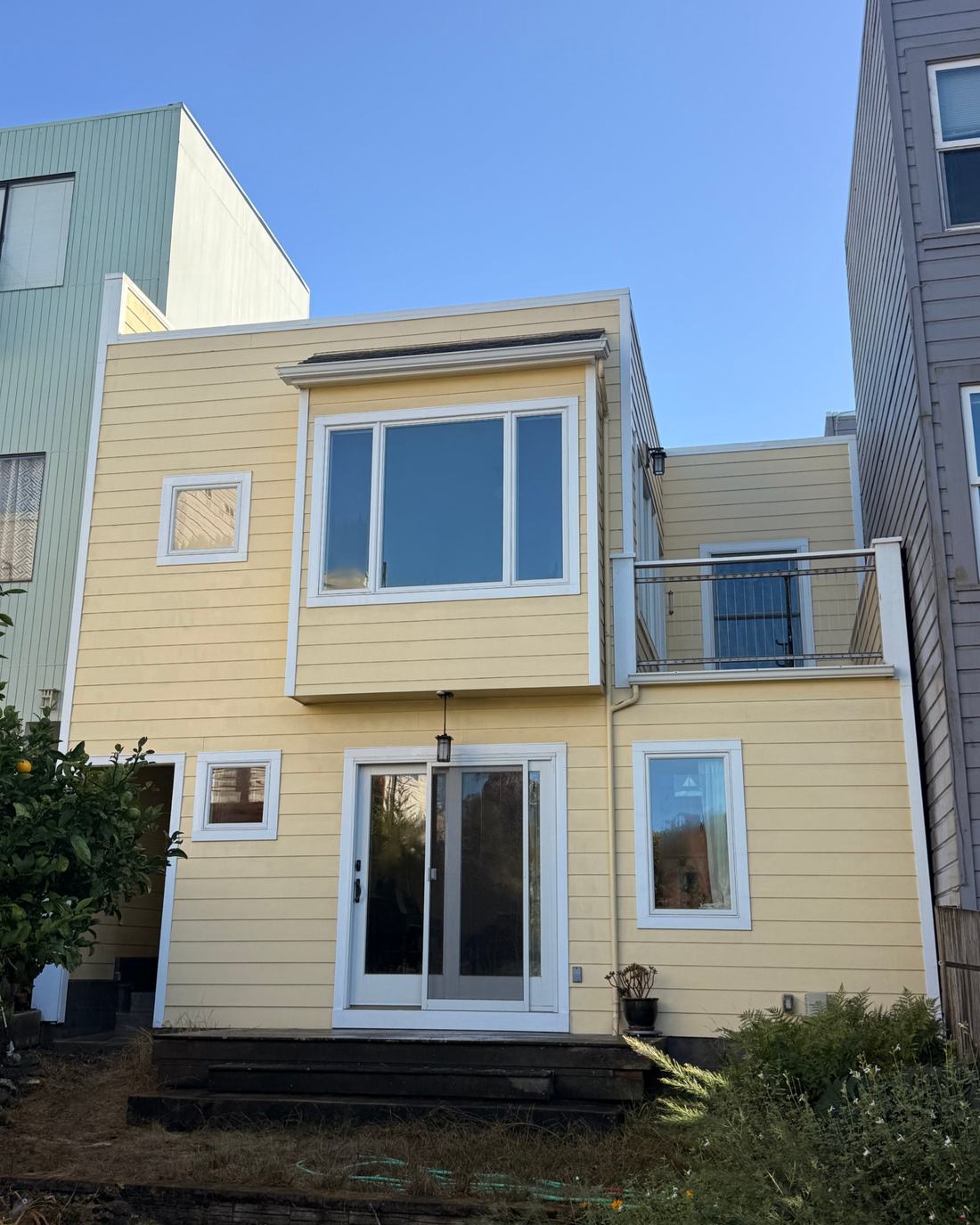 The same yellow house after soft washing, siding and white trim clean and even